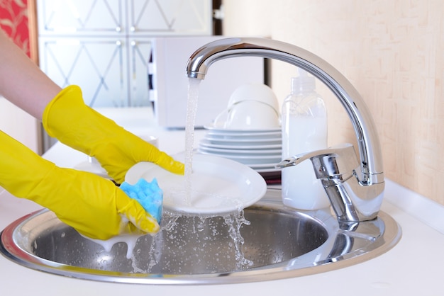 Cerrar las manos de mujer lavando platos en la cocina