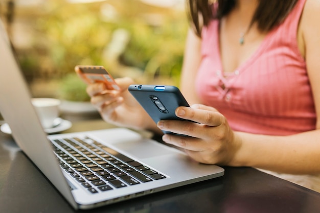 Foto cerrar las manos de la mujer sosteniendo la tarjeta de crédito mientras usa una computadora portátil y un teléfono móvil para comprar en línea