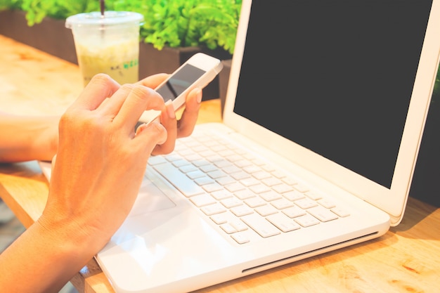 Cerrar las manos de la mujer usando teléfono inteligente y computadora portátil.