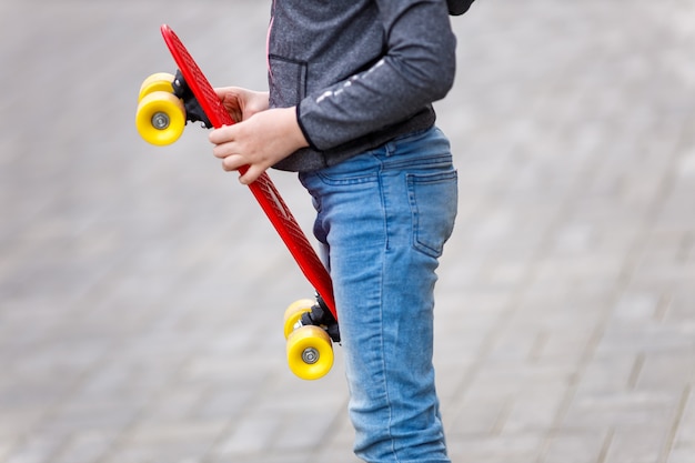 Cerrar las manos del niño sostiene una patineta roja en verano