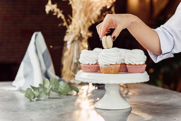 Cerrar las manos de repostería femenina pone un macarrón fresco encima de la magdalena con crema.