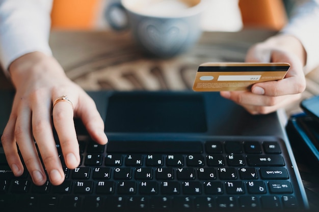 Cerrar las manos sosteniendo una tarjeta de crédito de plástico dorado y usando una computadora portátil. Concepto de compra online.