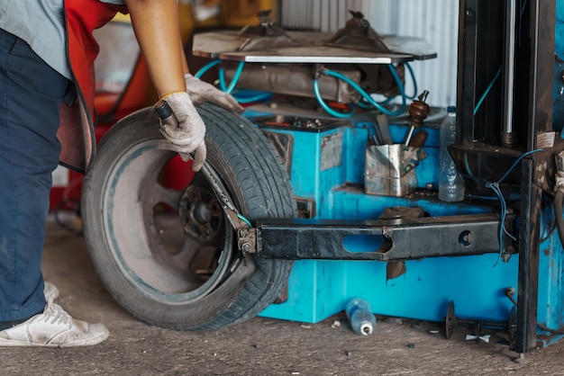 Cerrar Mecánico de automóviles reemplace el neumático en la rueda en el taller de servicio de reparación de automóviles.