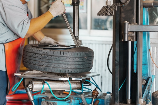 Cerrar Mecánico de automóviles reemplace el neumático en la rueda en el taller de servicio de reparación de automóviles.