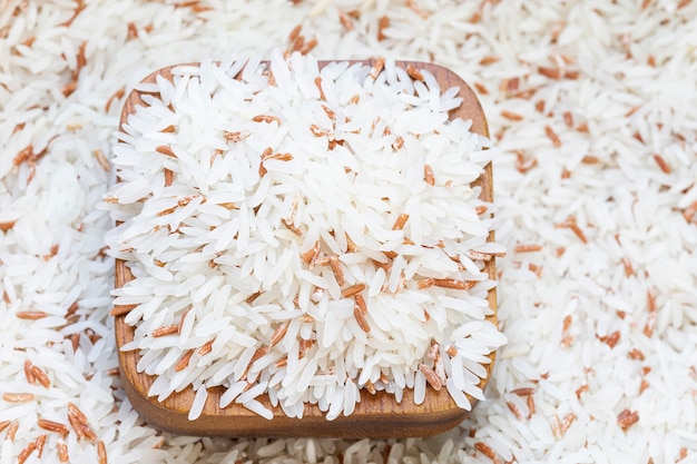 Foto cerrar mezcla de arroz blanco con arroz rojo en una taza de madera sobre fondo de arroz.