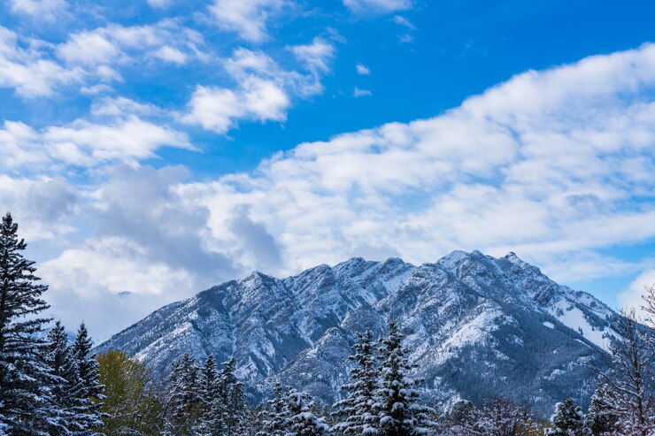 Cerrar el monte Norquay cubierto de nieve con bosque nevado sobre el cielo azul y las nubes blancas en invierno