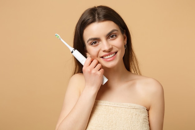 Cerrar morena mujer medio desnuda con una piel perfecta, maquillaje desnudo mantenga pincel aislado en la pared de color beige pastel