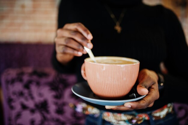 Cerrar mujer africana en suéter negro con taza de bebida caliente