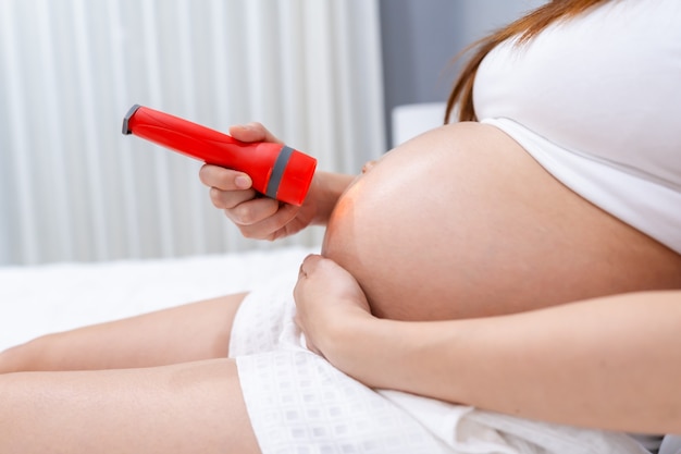 Cerrar mujer embarazada usando una linterna para jugar con el bebé en su vientre.