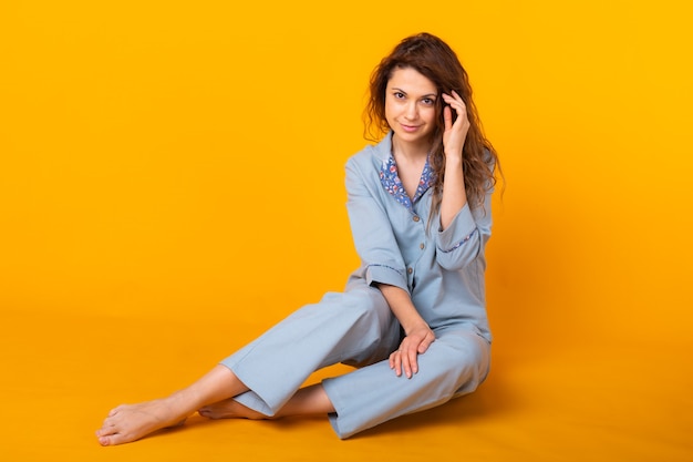 Cerrar una mujer joven en ropa de hogar azul. Aislado en la pared amarilla. Concepto de pijama.