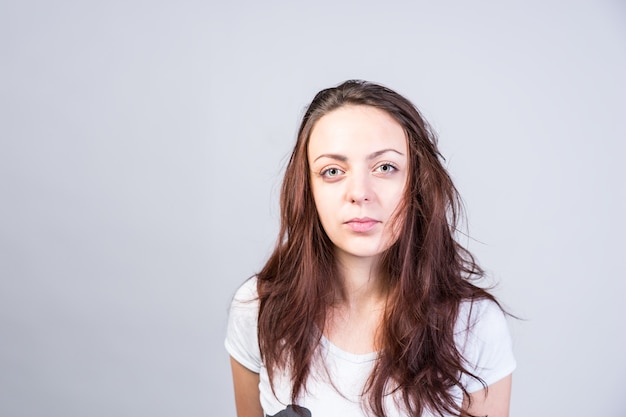 Cerrar mujer joven seria con cabello castaño largo desordenado mirando a cámara sobre un fondo gris.