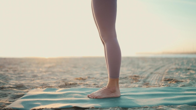 Cerrar mujer vistiendo polainas de pie en la estera de yoga Cerrar piernas femeninas en la playa