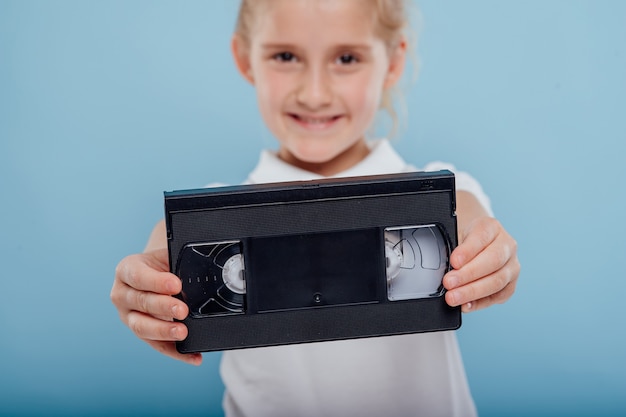 Foto cerrar niña con cinta de vídeo aislada sobre fondo azul aparatos antiguos