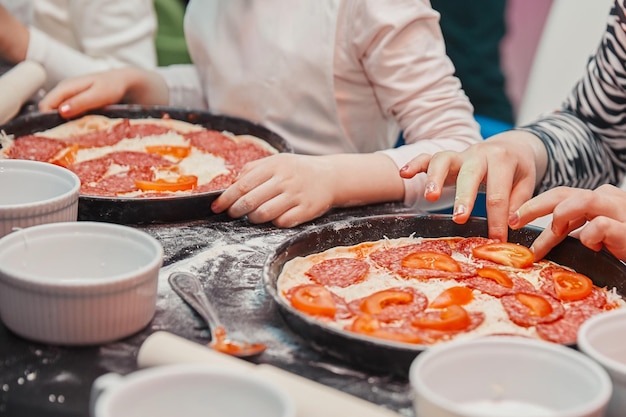 Cerrar una niña pone trozos de tomates sobre la base de pizza