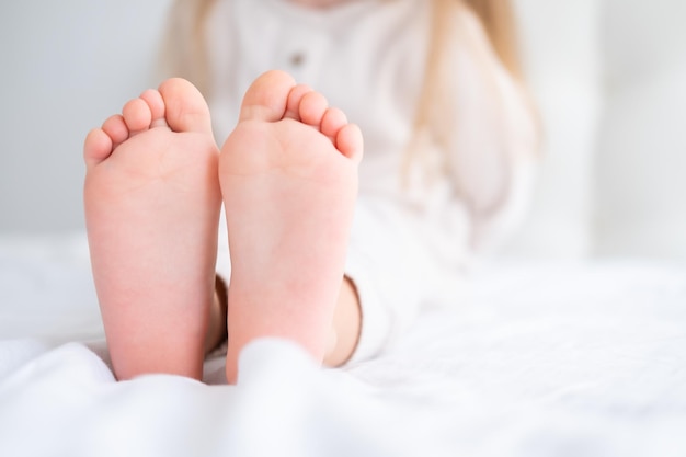 Cerrar niño niño descalzo piernas pies acostado sobre ropa de cama blanca Tonos de color claro pastel neutro