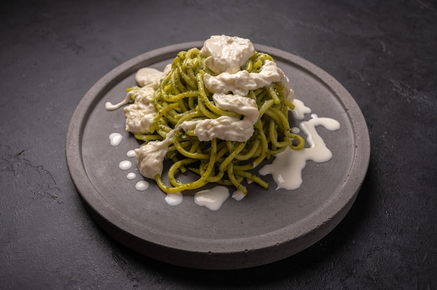 Cerrar la pasta con pesto, queso stracciatella servido en un plato de cerámica gris sobre fondo oscuro de grafit, enfoque selectivo