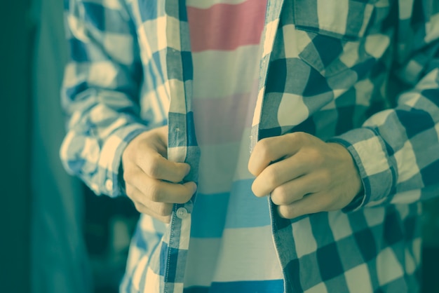 Foto cerrar persona ponerse y ajustar la camisa a cuadros en casa cerca del armario.