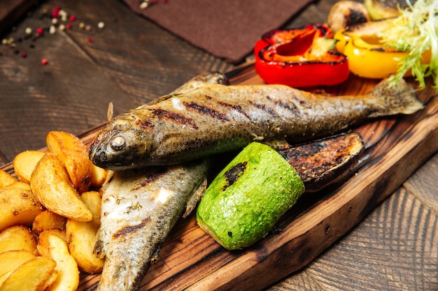 Cerrar el pescado a la plancha con verduras en la plancha de madera