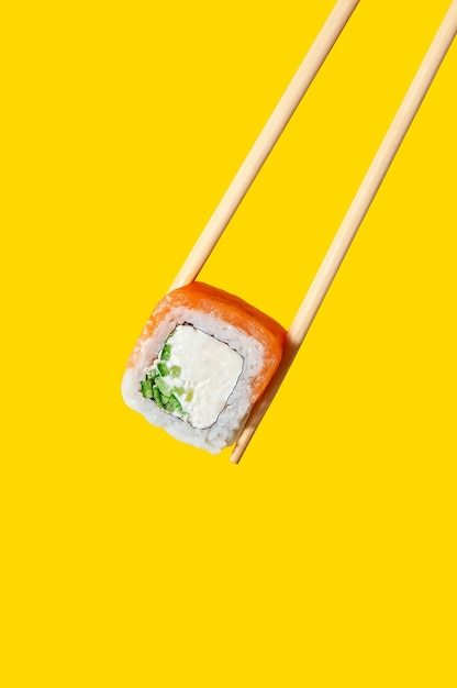 Cerrar Philadelphia Roll con salmón pescado, queso y pepino en palillos sobre fondo amarillo