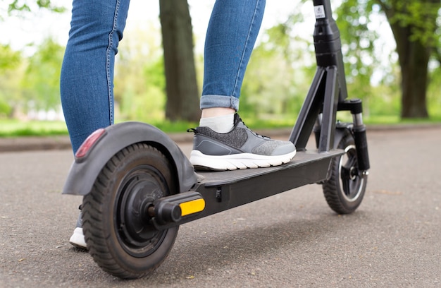 Cerrar las piernas de la mujer de pie sobre el patinete eléctrico en la vista trasera del día de verano a caballo.