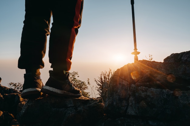 Cerrar las piernas de senderismo hombre de pie en la montaña con la luz del sol.