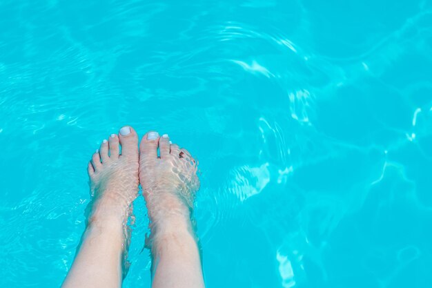 cerrar los pies de la niña en el agua de la piscinadía soleado de veranoagua de color azulmaqueta espacio para textomujer con