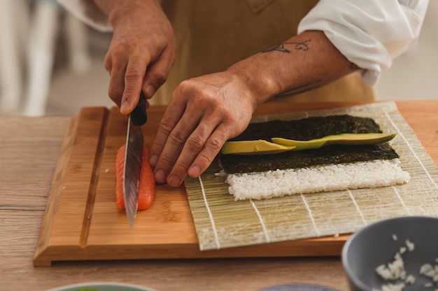 Cerrar preparar rollo de sushi en casa manos masculinas rebanar ingredientes salmón pepino aguacate y