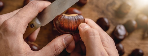 Cerrar el punto de vista desde la parte superior con las manos del hombre sosteniendo un cuchillo cortando castañas para cocinar en el fuego.