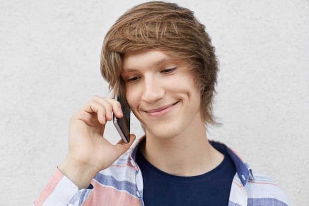 Cerrar retrato de adolescente guapo con peinado de moda, sonriendo suavemente con hoyuelos en las mejillas