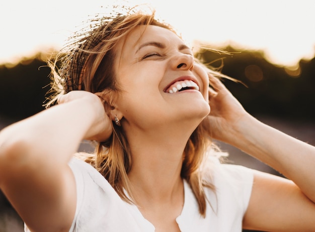 Cerrar el retrato de una bella mujer caucásica riendo con los ojos cerrados mientras sostiene su corona de lavanda contra la puesta de sol.