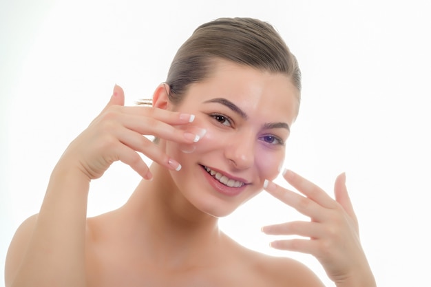 Foto cerrar el retrato de la belleza de una hermosa mujer riendo aplicando crema facial y mirando aislado