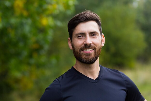 Cerrar retrato joven barbudo feliz de pie en la naturaleza entre los árboles del bosque se relaja, respira aire fresco y cierra los ojos. Hombre disfruta de una vida de paz tranquila, tranquila en el parque. Al aire libre. Felicidad