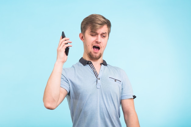 Cerrar retrato joven enojado, chico estudiante loco gritando por teléfono sobre azul