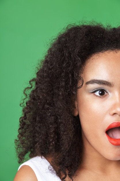 Cerrar el retrato de media cara de una mujer africana bastante joven con maquillaje, mirando a otro lado aislado sobre verde