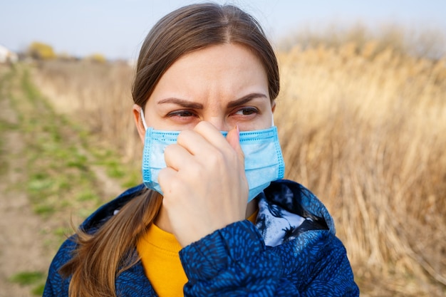 Cerrar retrato mujer al aire libre en mascarilla quirúrgica con correas de goma para los oídos. Mascarilla quirúrgica típica de 3 capas para cubrir la boca y la nariz. Máscara de procedimiento de bacterias. Concepto de protección.