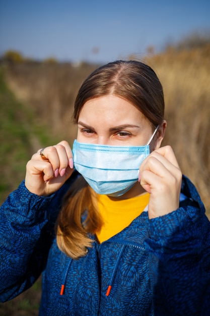 Cerrar retrato mujer al aire libre en mascarilla quirúrgica con correas de goma para los oídos. Mascarilla quirúrgica típica de 3 capas para cubrir la boca y la nariz. Máscara de procedimiento de bacterias. Concepto de protección.