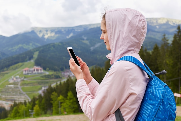 Cerrar retrato de perfil de excursionista joven con mochila azul con smartphone en el hermoso paisaje de montaña en primavera