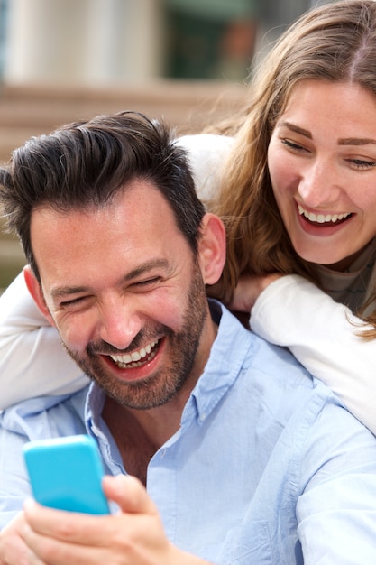 Cerrar riendo pareja sentados juntos en abrazo con teléfono móvil