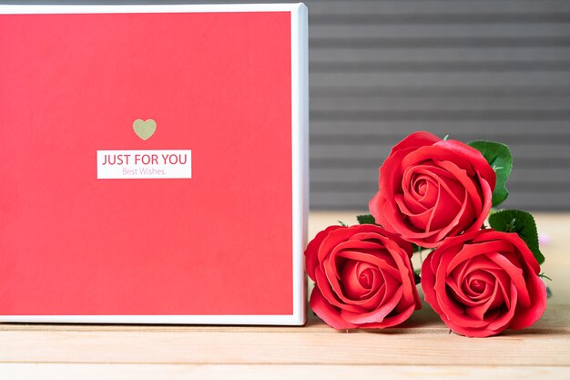 Cerrar rosas rojas y caja en forma de corazón sobre fondo de madera, concepto del Día de San Valentín con rosas y caja roja en forma de corazón