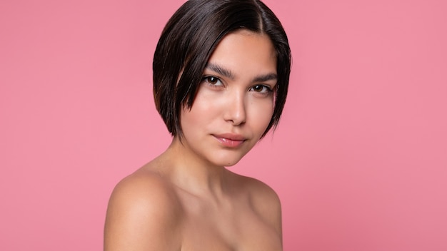 Cerrar el rostro de la hermosa mujer joven con una piel limpia perfecta. Retrato de modelo de belleza con maquillaje nude natural. Spa, cuidado de la piel y bienestar. Fondo de coral melocotón rosa. Formato panorámico 16: 9.