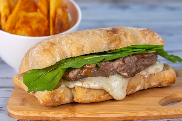 Cerrar sándwich de carne con queso y rúcula en pan ciabatta servido con papas fritas