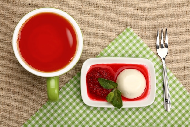 Cerrar sirviendo panna cotta postre italiano tradicional con mermelada de frambuesa y una taza de té negro rojo