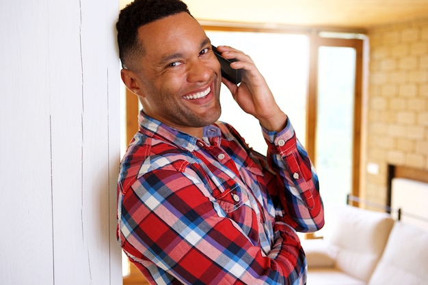 Cerrar sonriente joven afroamericano hablando por teléfono inteligente en casa