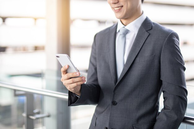 Foto cerrar la sonrisa del hombre de negocios asiático joven que sostiene el teléfono inteligente en el área de la oficina