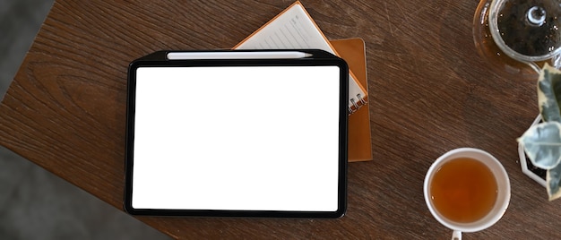 Cerrar en tableta digital con pantalla en blanco, taza de té caliente y cuaderno o mesa de madera