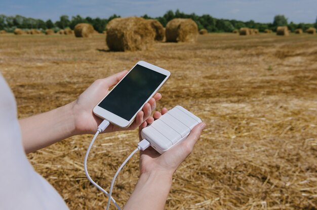 Cerrar en el teléfono móvil en blanco con el banco de energía en la mano