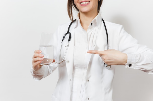 Cerrar tiro recortada mujer sonriente médico con estetoscopio aislado sobre fondo blanco. Doctora en bata médica apuntando a un vaso de agua. El personal sanitario, la salud, el concepto de medicina.