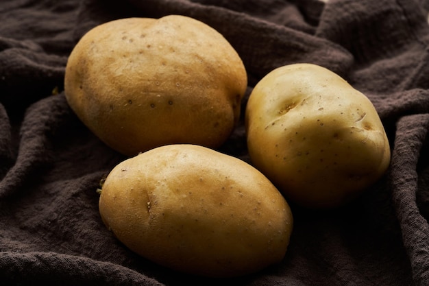 cerrar tres patatas crudas sobre tela marrón. fondo del concepto de comida