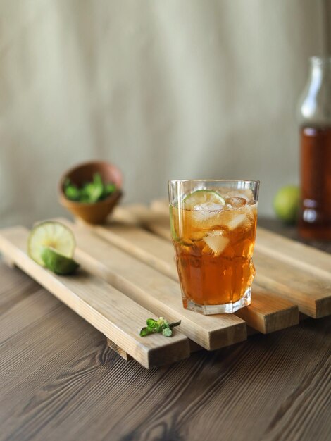 Cerrar un vaso de té frío con cubitos de hielo y lima en una mesa de madera