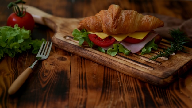 Cerrar vista de comida de desayuno con croissant sandwich jamón y queso en bandeja de madera